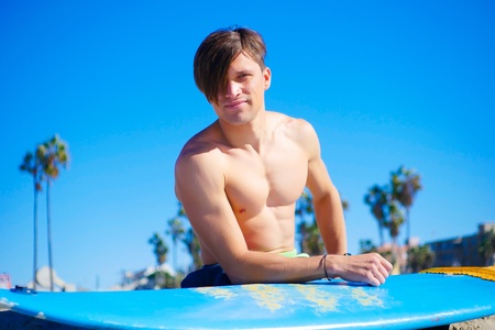Portrait of a model young male hold surfboard, modern hairstyle, bright blue dayの写真素材