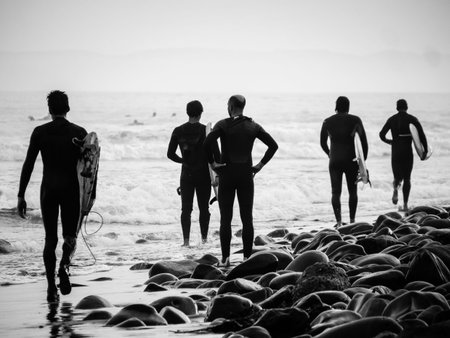 Mid age surfers walking on stone beach, sport changing lives. Black and white photo