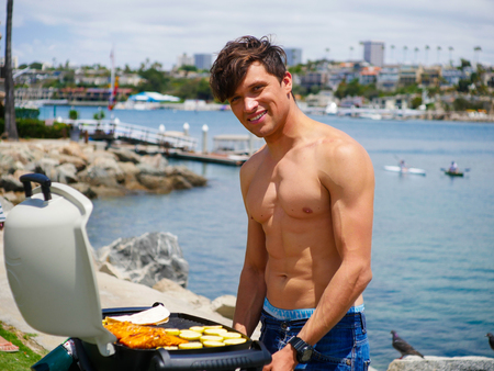 Young men cooking barbecue outdoor, handsome model, shirtless male with 6 packs. Gas grill barbecue concept. Holiday bbq party ideas.の写真素材