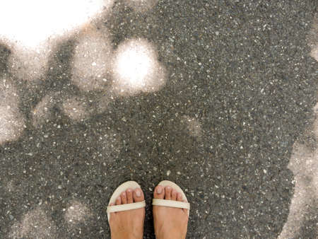 woman's feet on the road floor with shadow of trees and sunlightの写真素材