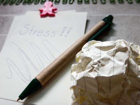 Crumpled paper balls and sheet of paper with stress word and penの写真素材