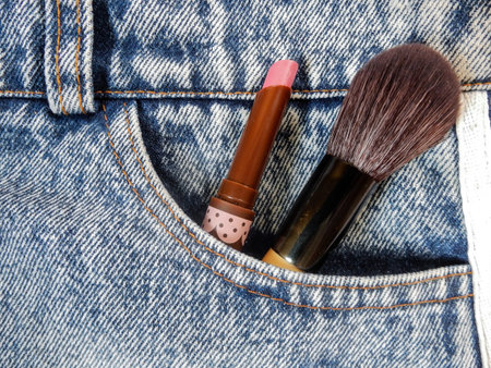 blue faded jeans  closeup with cosmetic equipment is brush and lipstick in front pocketの写真素材