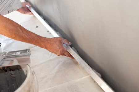 Closeup of repairman hand plastering a wall with long trowelの写真素材