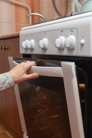 Close up of women hand opening the oven door to control the roast in the gas stoveの写真素材