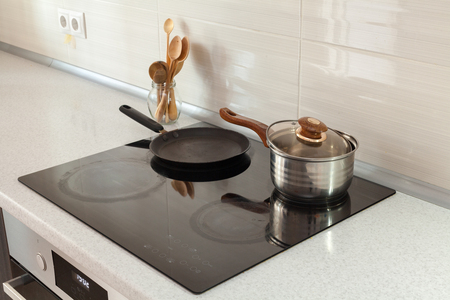 Open saucepan, pan and wooden spoons in modern kitchen with induction stoveの写真素材