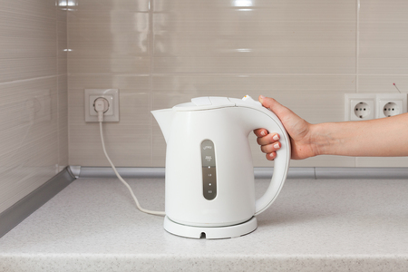 Electric Kettle in hand on the background of the kitchen.の写真素材