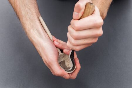 Man hands carving of a wooden spoon with hook knife on gray backgroundの写真素材