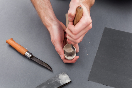 Man hands carving of a wooden spoon with hook knife on gray background with emeryの写真素材
