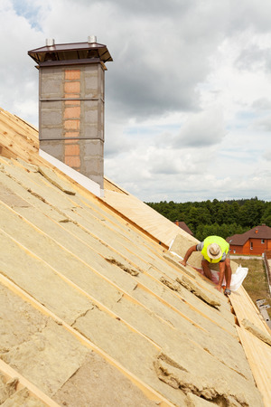 Roofer builder worker installing roof insulation material (rockwool) on new house under constructionの写真素材
