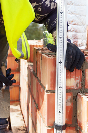 Construction mason worker measures the thickness of the seams on the brickの写真素材