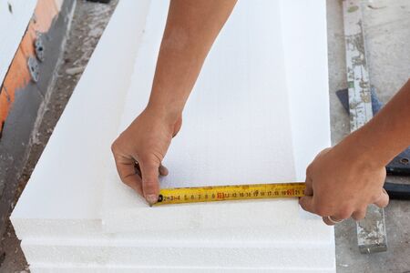 Thermal insulation house foundation walls with styrofoam boards. Worker use ruller to measure the  correct length of styrofoamの写真素材
