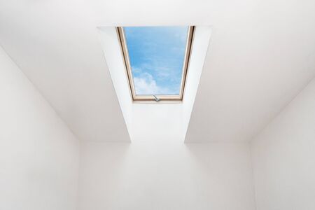 A modern open skylight (mansard window) in an attic room against blue skyの写真素材