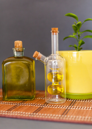 Two glass bottles olive oil stands near a flower against a dark backgroundの写真素材
