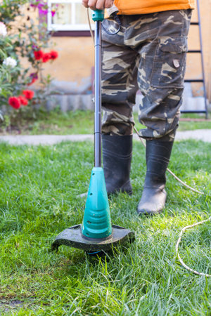 Man in rubber boots with a mower in front of back yard