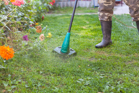 Man in rubber boots with a mower in front of back yardの写真素材