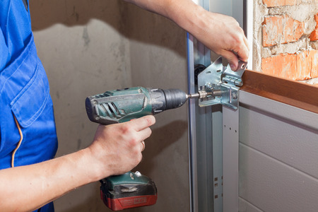 Garage doors installation.Worker installing  lifting system in metal profil with screwdriverの写真素材