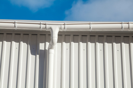 New white rain gutter on a building with white metal sheet against blue skyの写真素材