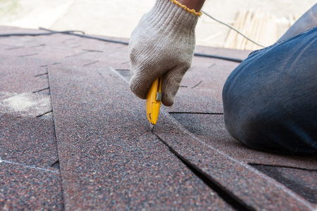 Roofer worker cuts shingles on the roofの写真素材