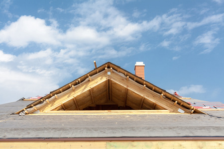 New frame house under construction. Roof with asphalt shingles, chimney and insulation materialの写真素材