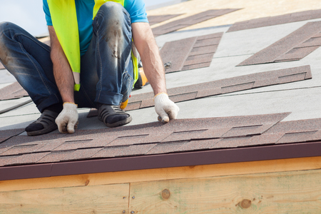 Roofer builder worker installing  Asphalt Shingles or Bitumen Tiles on a new house under constructionの写真素材
