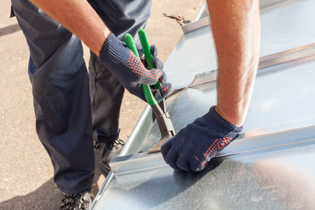 Roofer builder worker finishing folding a metal sheet using special pliers with a large flat gripの写真素材