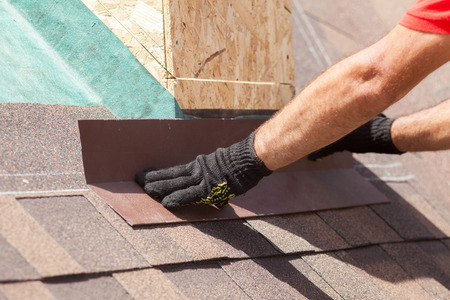 Roofer builder worker installing shingles on a new wooden roof with skylightの写真素材