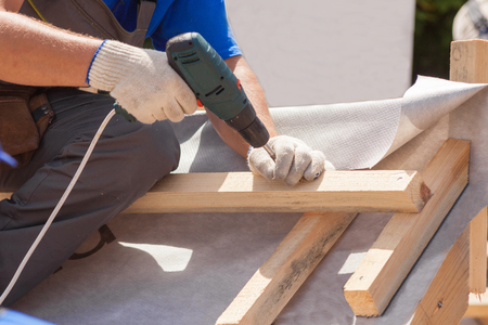 Skylight installation. Roofer builder worker use skrewdriver to fasten a wooden beamの写真素材