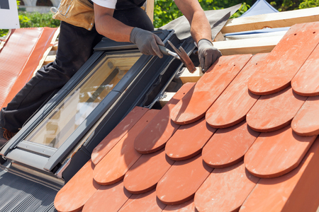 Hands of roofer laying tile on the roof. Installing natural red tile using hammerの写真素材