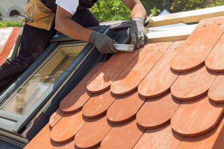 Natural roof tile instaalation. Roofer builder worker use ruller to measure the distance between the tiles.  Roof with mansard windows.の写真素材