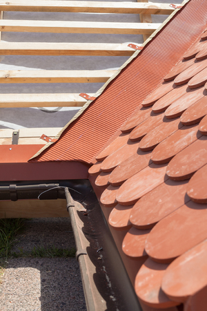 New roof under construction with wooden beams, waterproofing layer for corner and natural tileの写真素材
