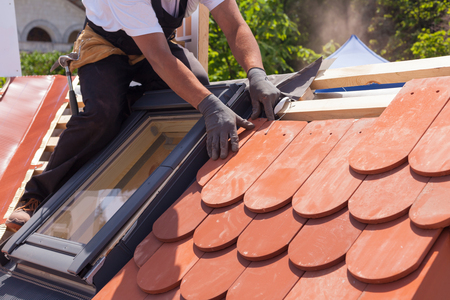 Hands of roofer laying tile on the roof. Installing natural red tile.の写真素材