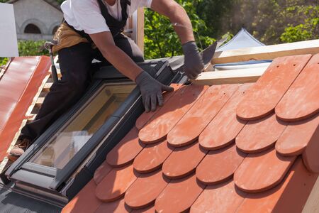 Hands of roofer laying tile on the roof. Installing natural red tile.の写真素材
