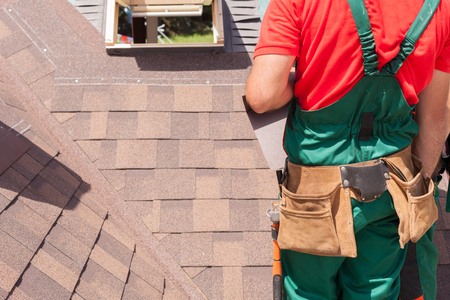 Roofer builder worker with bag of tools installing roofing shinglesの写真素材