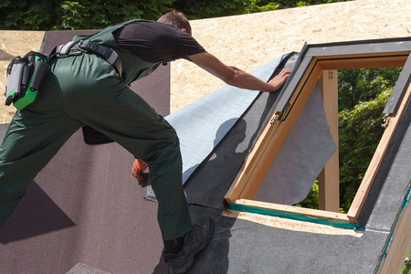 Roofer builder worker installing heating and melting bitumen roofing felt. Skylight. Roof window.の写真素材