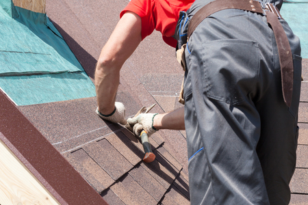 Roofer builder worker use a hammer for installing roofing shinglesの写真素材