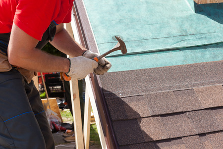 Roofer builder worker use a hammer for installing roofing shinglesの写真素材