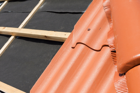 New roof under construction with wooden beams, waterproofing layer for corner and natural tileの写真素材