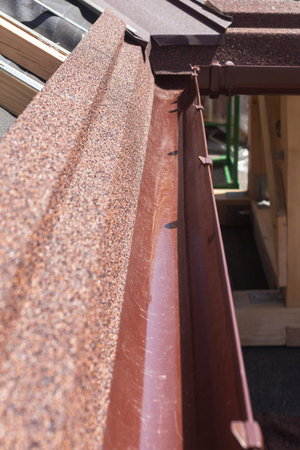 New asphalt shingle roof with brown rain gutter, wooden beams and vapour control layerの写真素材
