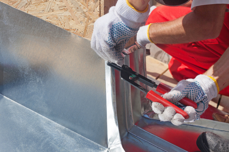 Roofer builder worker finishing folding a metal sheet using special pliers with a large flat gripの写真素材