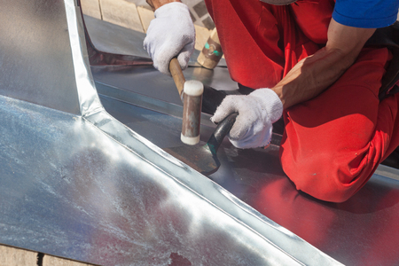 Roofer builder worker finishing folding a metal sheet using rubber malletの写真素材