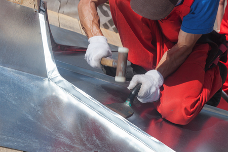 Roofer builder worker finishing folding a metal sheet using rubber malletの写真素材