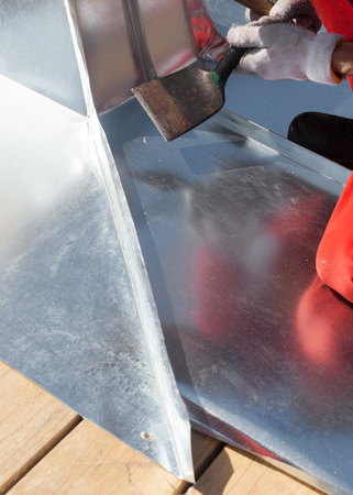 Roofer builder worker finishing folding a metal sheet using rubber malletの写真素材
