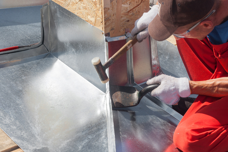 Roofer builder worker finishing folding a metal sheet using rubber malletの写真素材