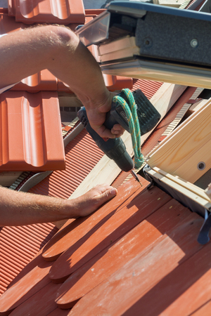 Roofer installs a skylight on the new roof using a drillの写真素材