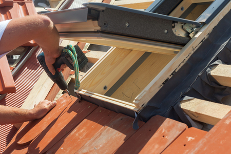 Roofer installs a skylight on the new roof using a drillの写真素材