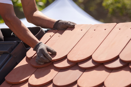 Hands of roofer laying tile on the roof. Installing natural red tile.の写真素材