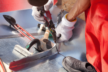 Roofer builder worker finishing folding a metal sheet using metal shearsの写真素材