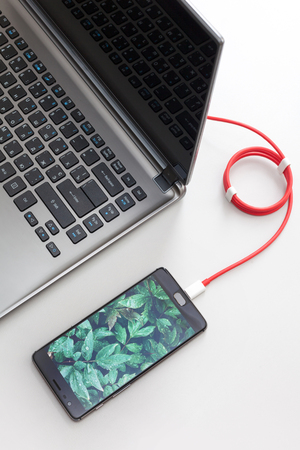 Workspace with smartphone with green plants screen is connecting to laptop computer on white deskの写真素材