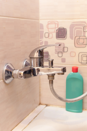 Closed water tap in the bathroom. Bottle of cleaning detergent for bathroom applies a scour to the metal water tap.の写真素材