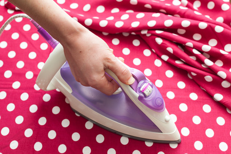 Female hand ironing clothes top view during housework. Close-up of maid hand ironing clothes on ironing board at homeの写真素材
